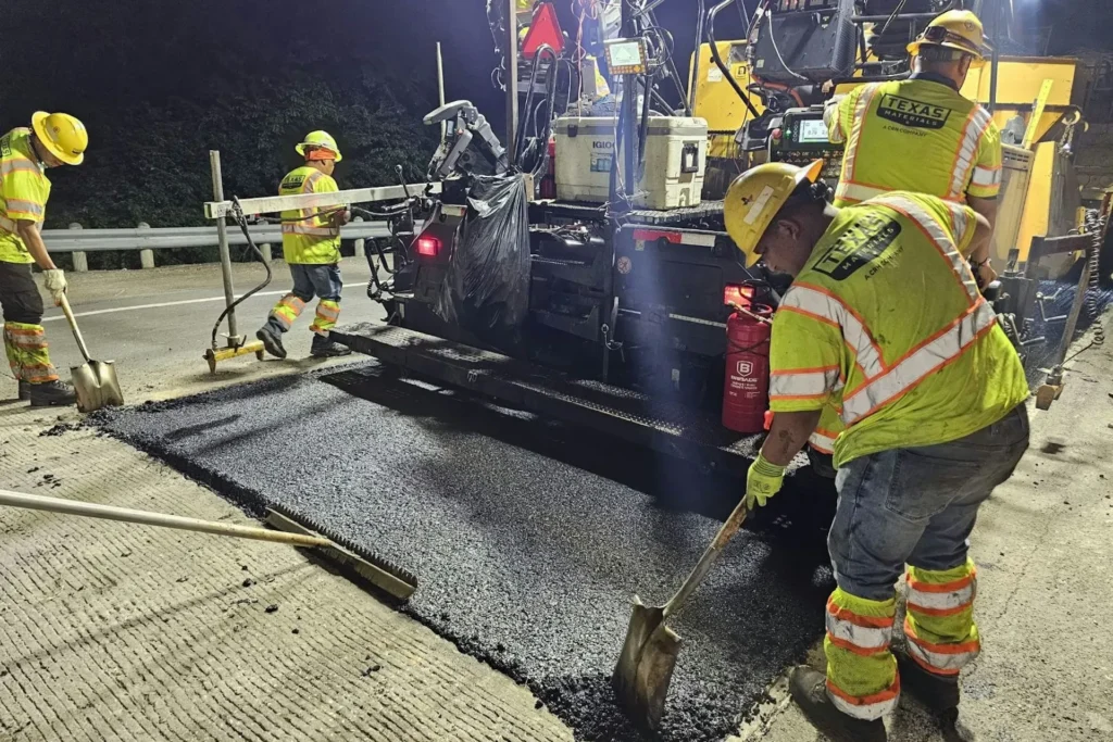 Asphalt paving crew in high visibility gear laying hot asphalt at night