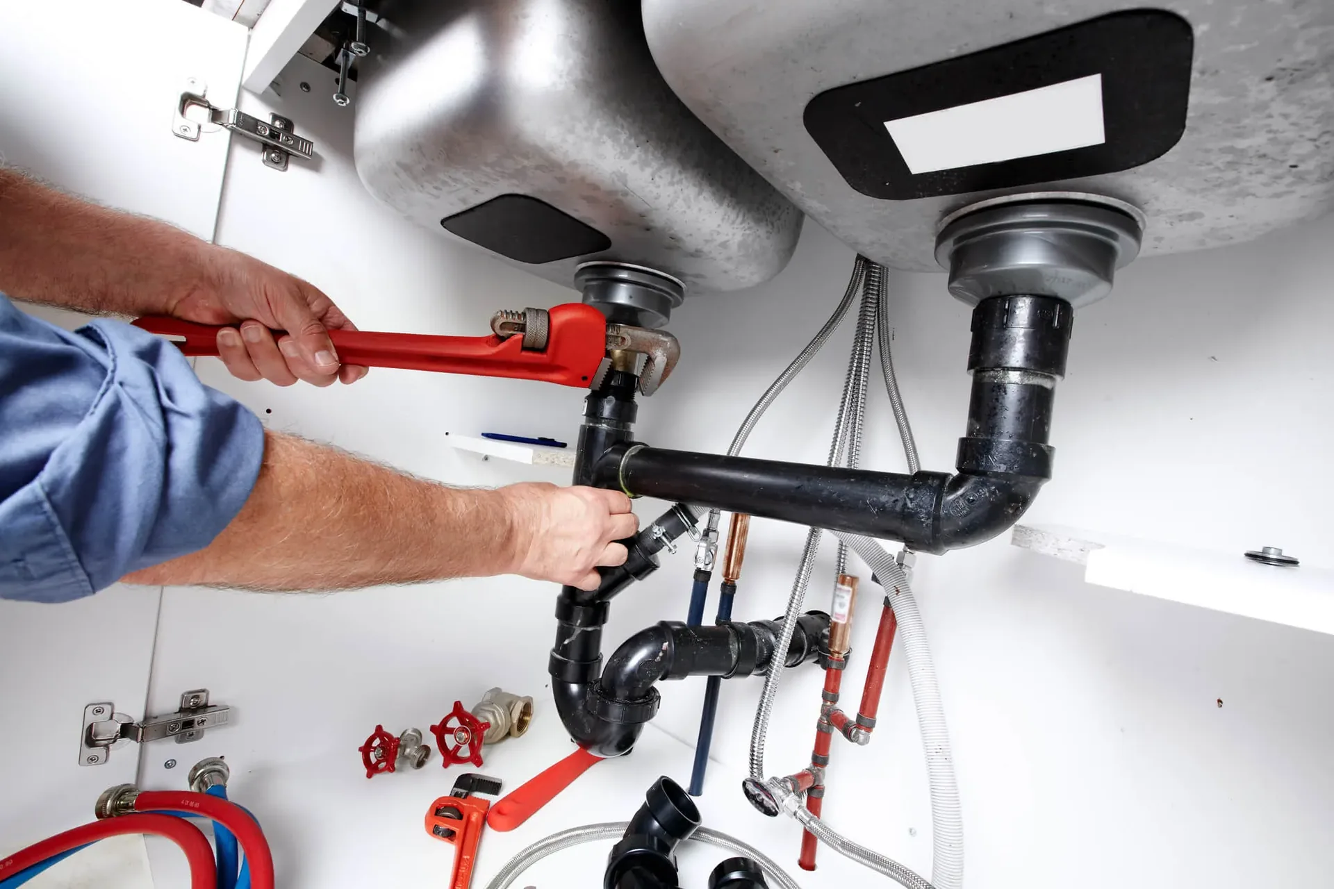 Plumber tightening pipework beneath a sink with a pipe wrench