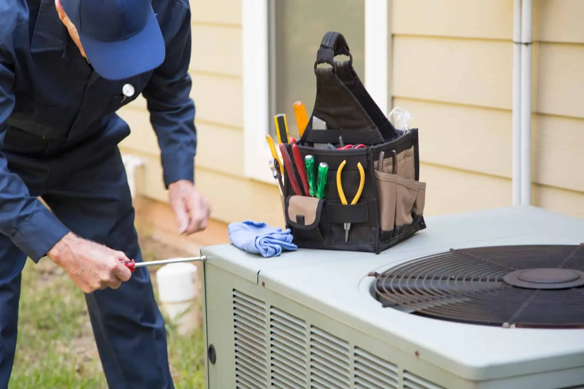 HVAC technician with tools servicing an outdoor air conditioning unit