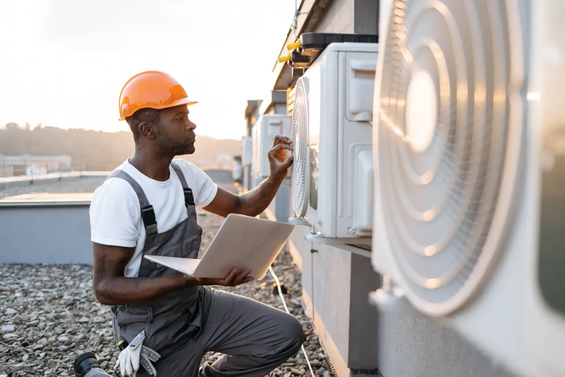 HVAC technician with a laptop servicing rooftop condenser units