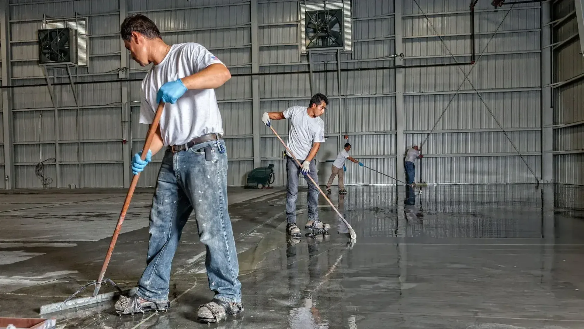 Flooring crew spreading epoxy coating across a large warehouse floor