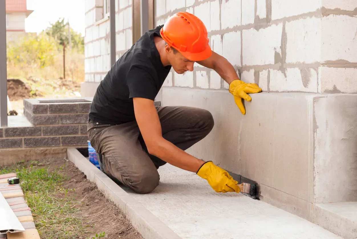 Worker sealing and waterproofing a block foundation wall