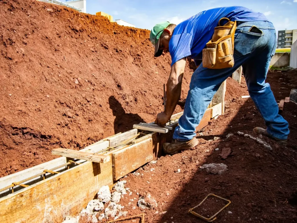 Foundation repair technician working in an excavated trench beside a house