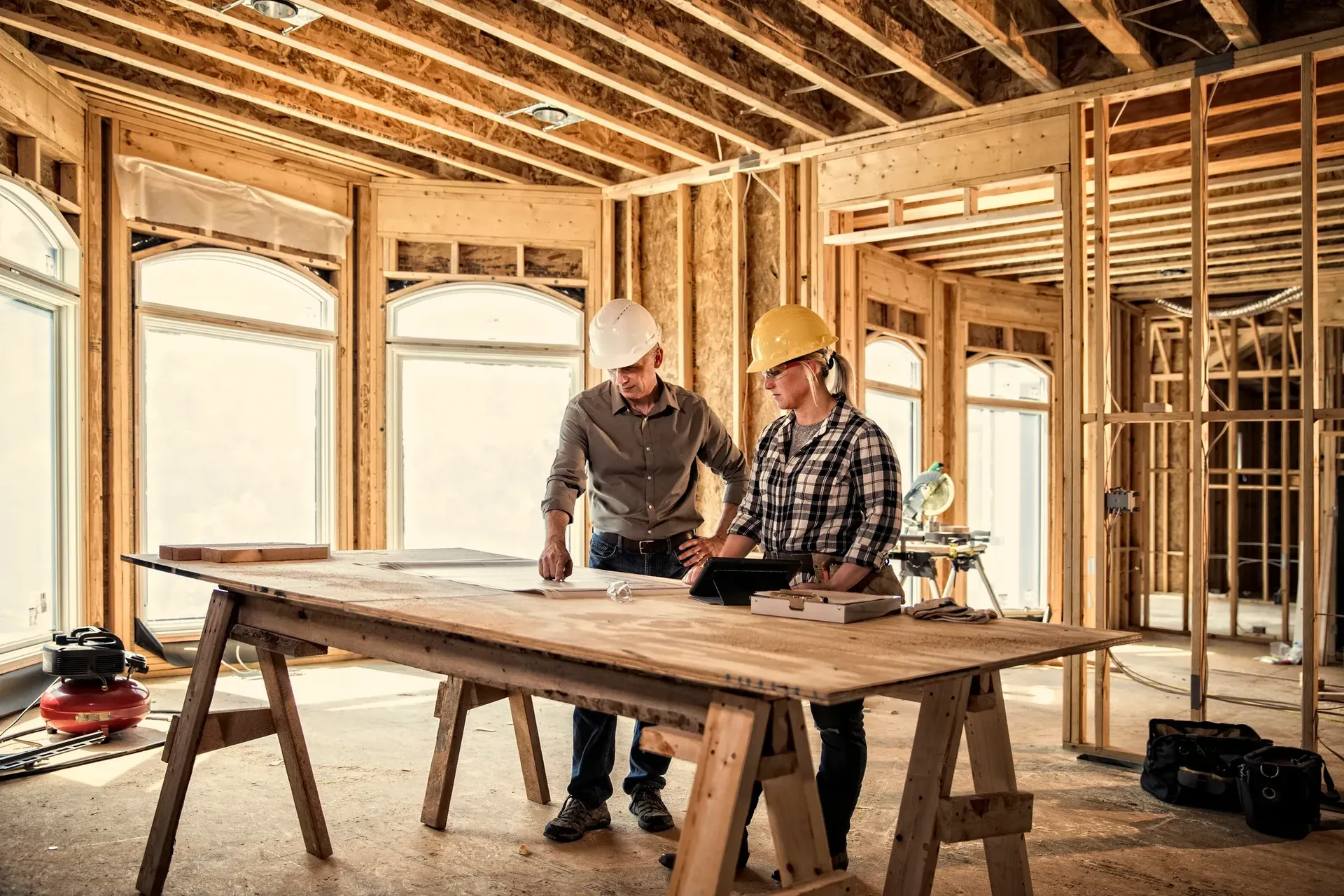 Two general contractors reviewing blueprints inside a framed building