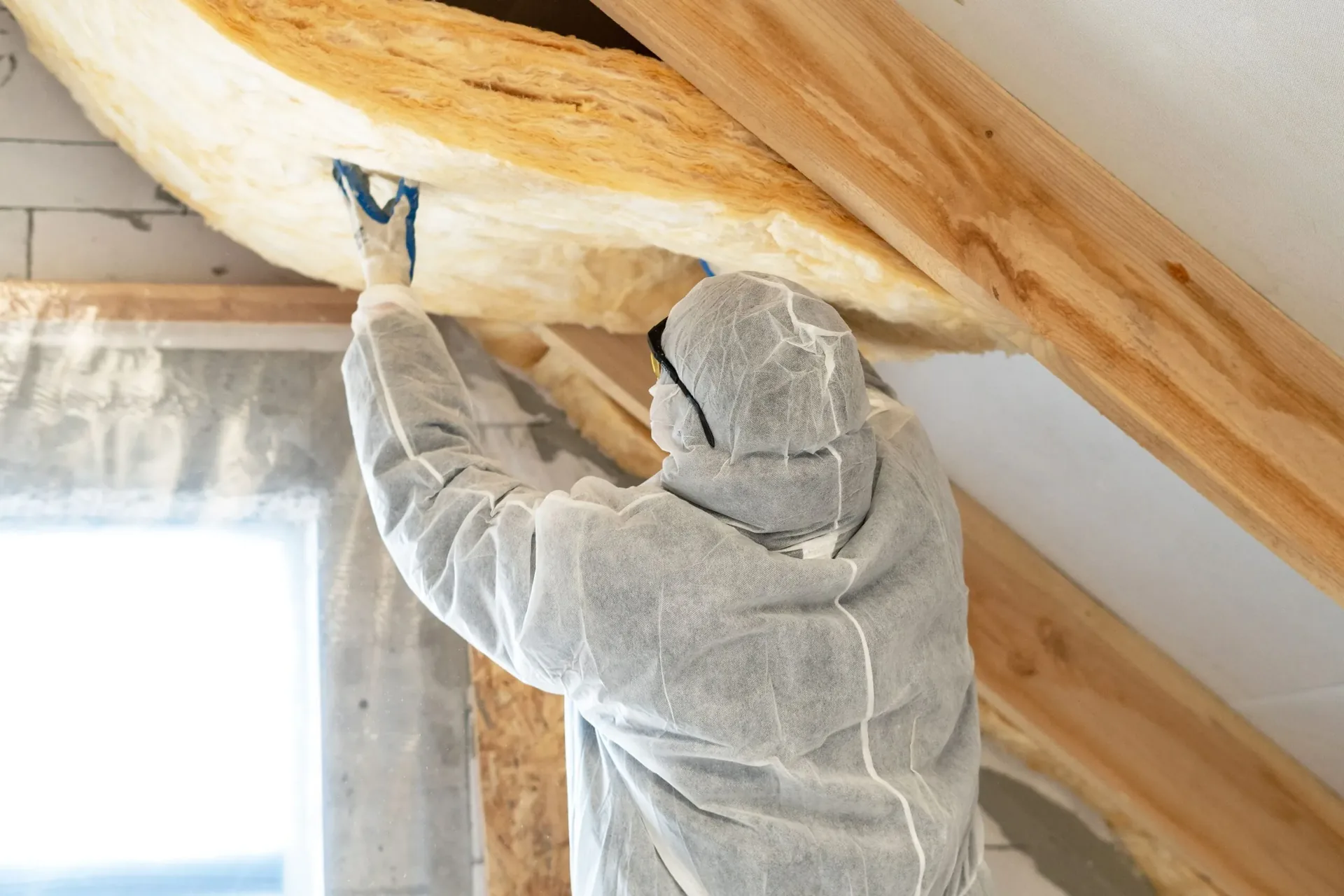 Technician in protective gear spraying foam insulation onto a ceiling