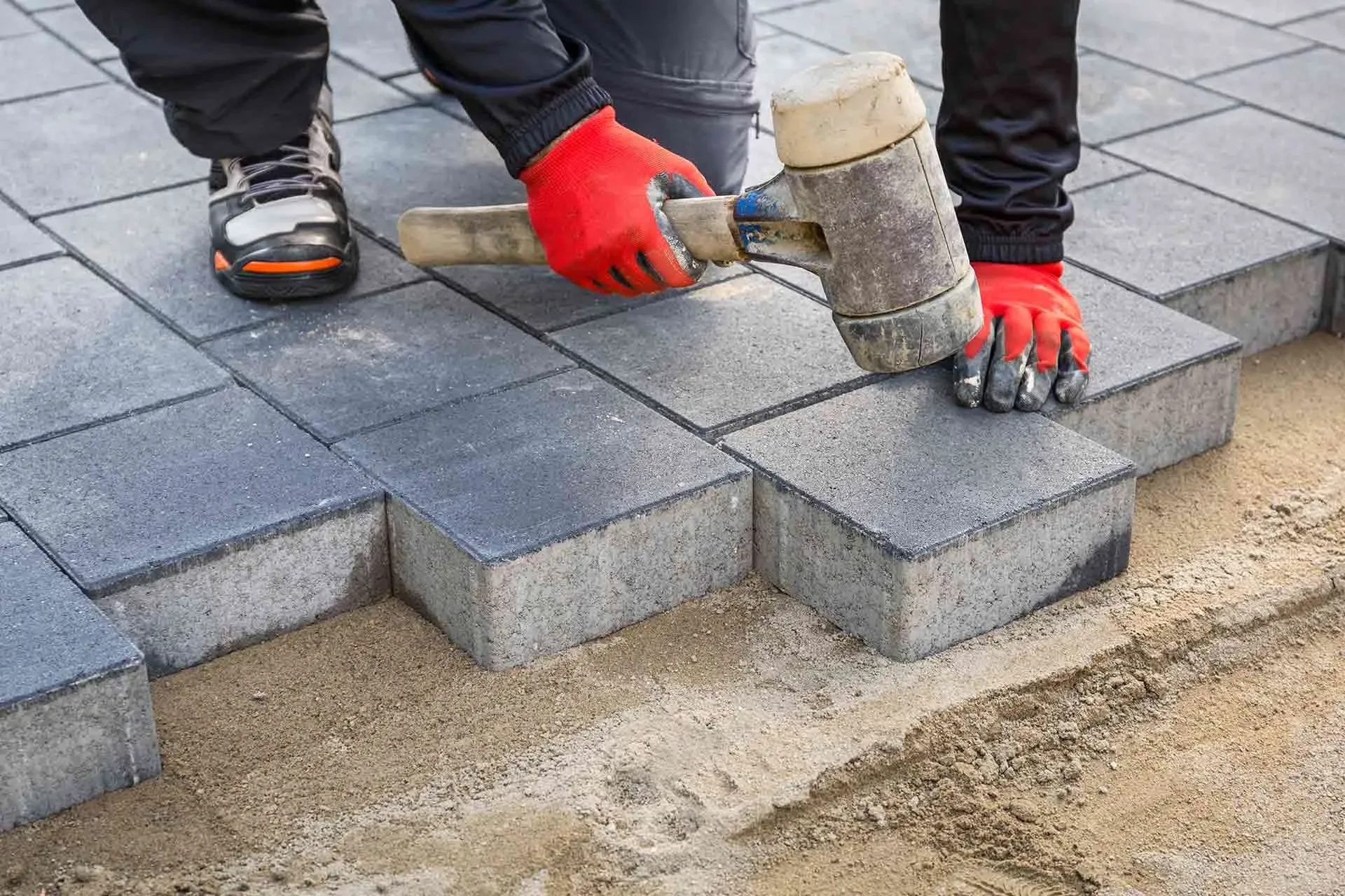 Worker laying and aligning block pavers on a prepared base