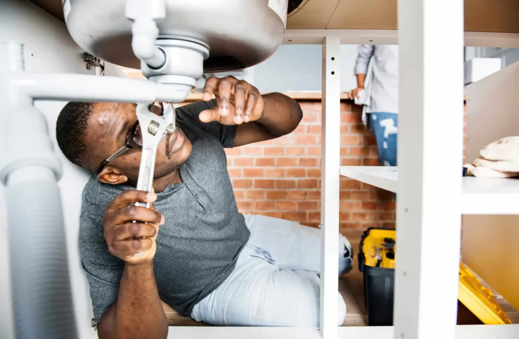 Plumber lying under a sink tightening a pipe fitting with a wrench