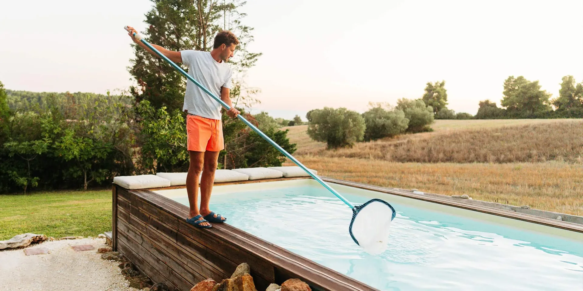 Worker cleaning a backyard swimming pool with a long handled net