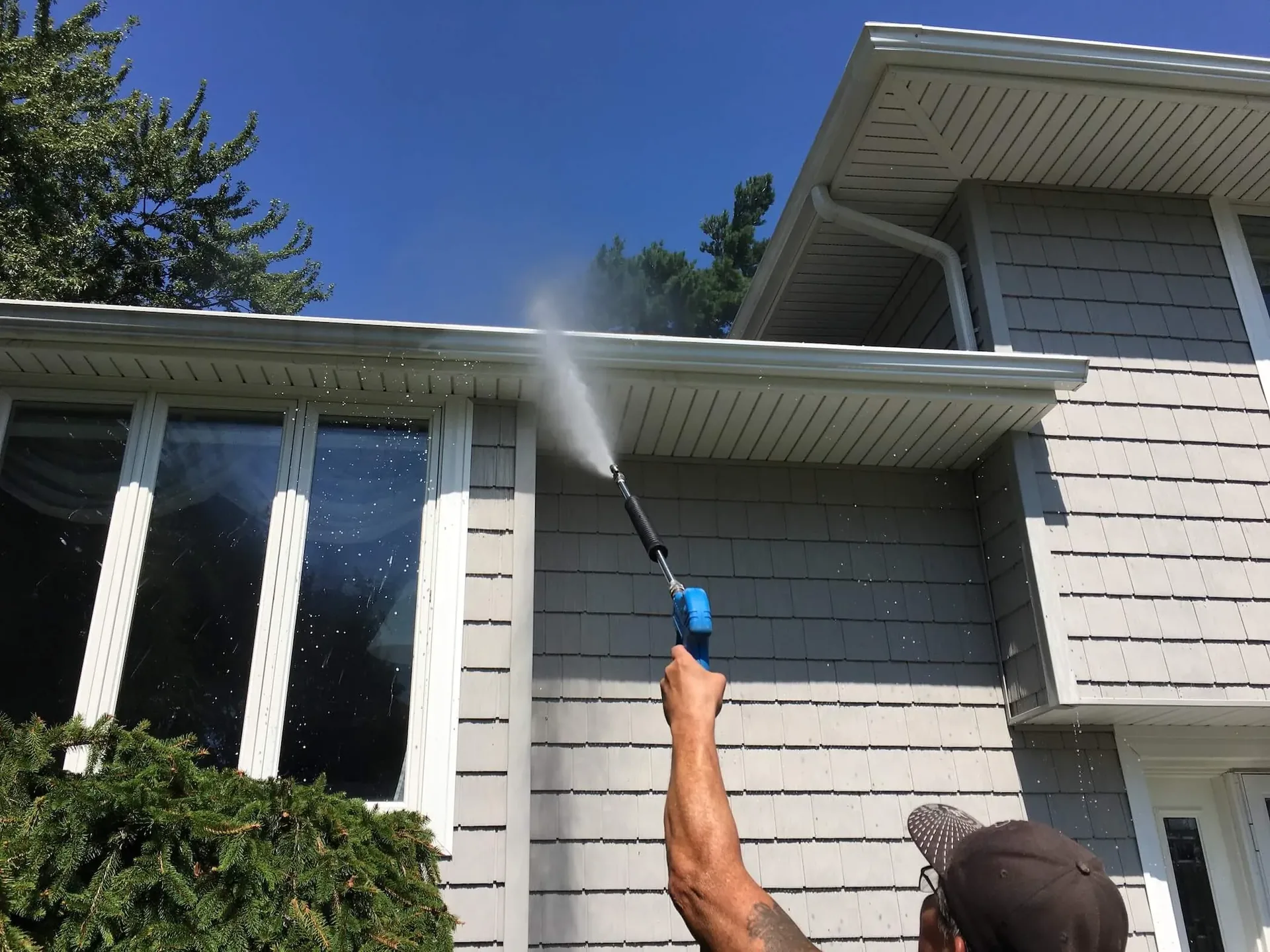 Worker pressure washing the exterior wall and trim of a house