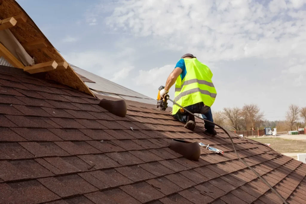 Roofer in a safety vest installing asphalt shingles on a residential roof